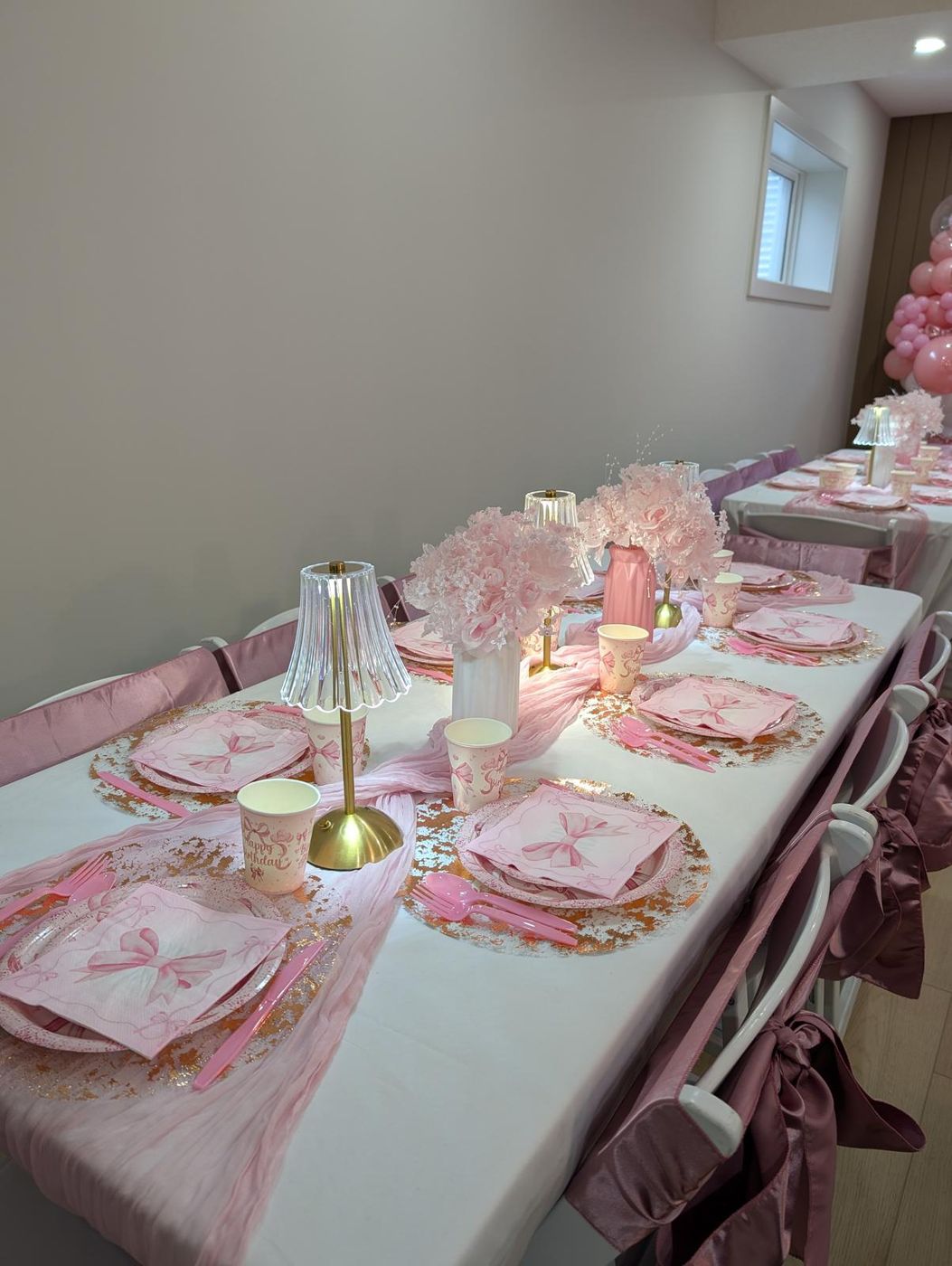 Pink bow-themed backdrop with balloon garlands, drapery and marquee numbers